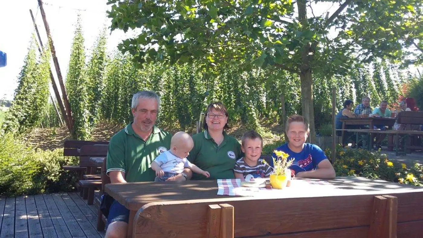 Familie Ehrensperger am Holztisch im Gastgarten vor dem Hopfengarten