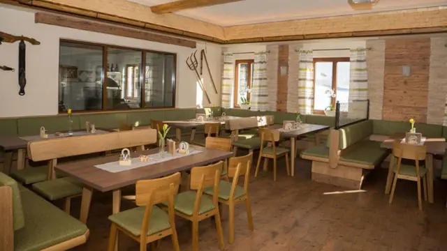 Stube mit Holztischen, grünen Polsterbänken und Blumen am Tisch